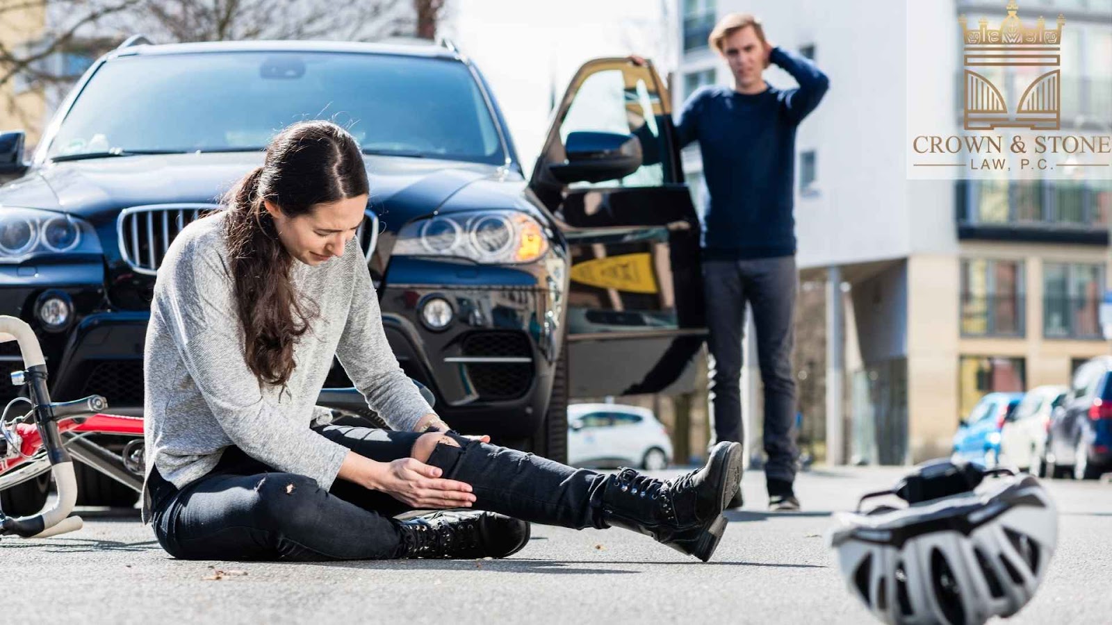 Injured cyclist sitting near car accident scene.